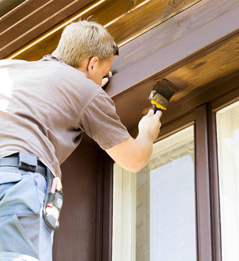 Man painting window frame on home exterior